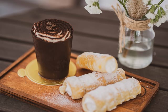 Domácí kremrole s bohatou náplní a čokoládový dezert podávaný na dřevěném podnosu v kavárně V Klenbách.