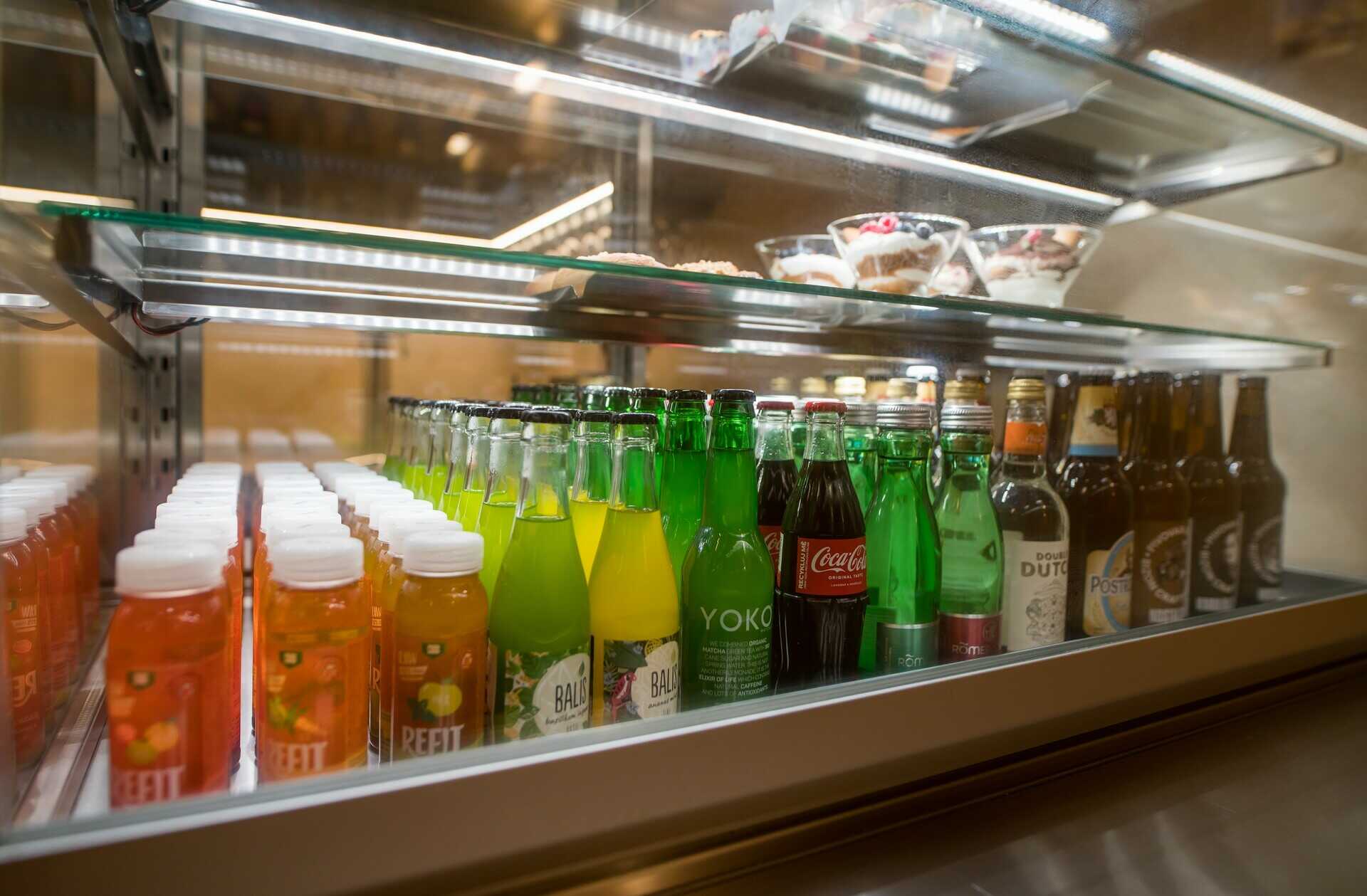 Sortiment chlazených nealkoholických nápojů, ovocných moštů a limonád v prosklené chladničce baru.