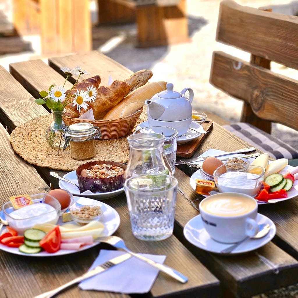 Snídaňové menu s kávou a pečivem podávané na dřevěném stole venkovní zahrádky v historickém centru.