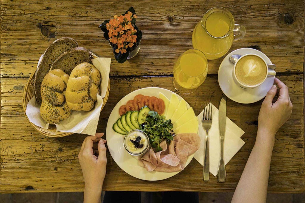 Snídaňový talíř s uzeninami, sýry, zeleninou a čerstvou kávou připravený pro hosty ubytování.
