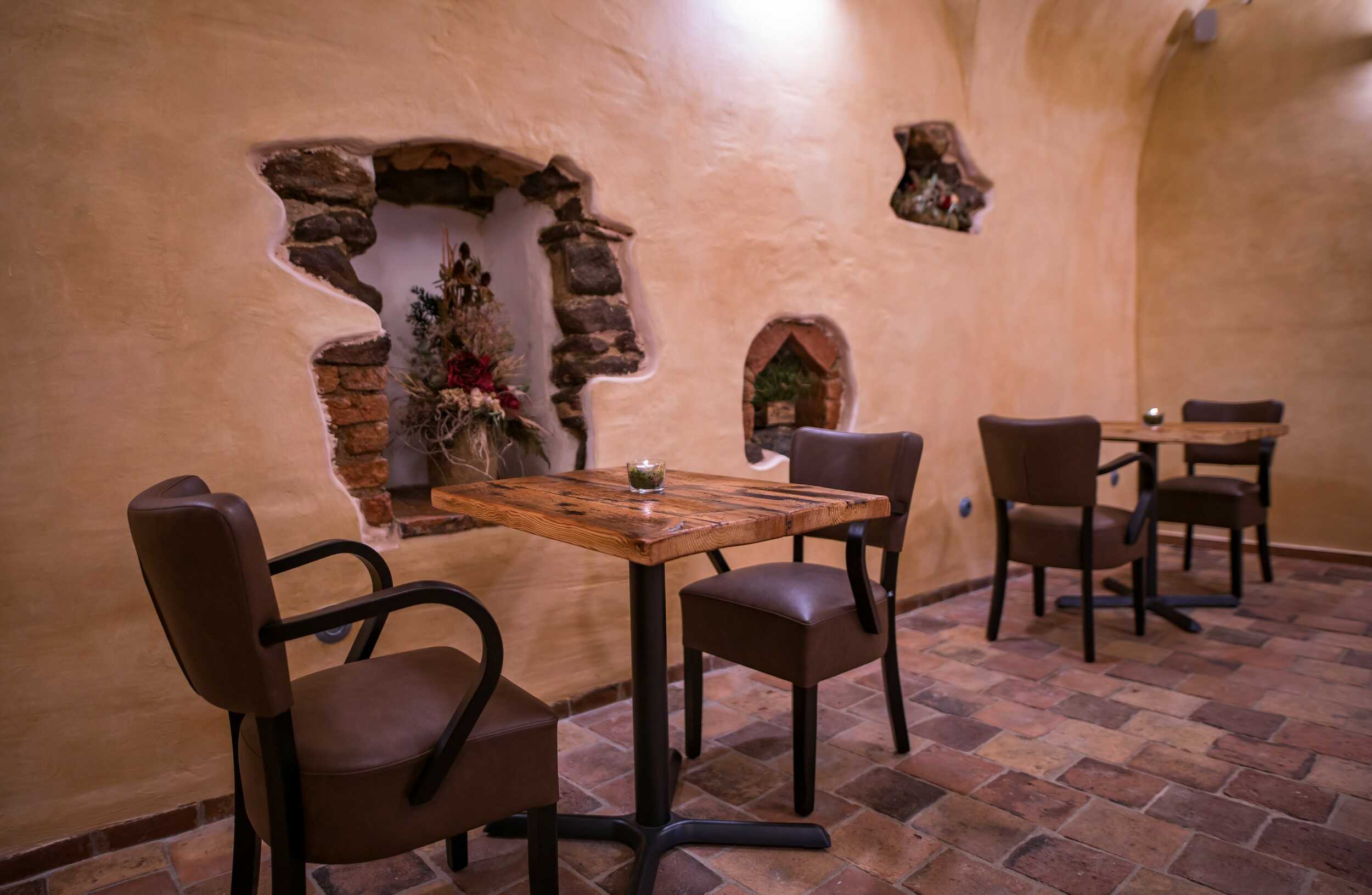 Stůl s koženými křesílky umístěný v osvětlené kamenné nice renesančního domu.