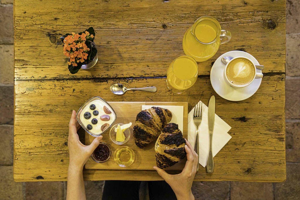 Pohled shora na ranní menu sestávající z máslového croissantu, domácího jogurtu a výběrové kávy.