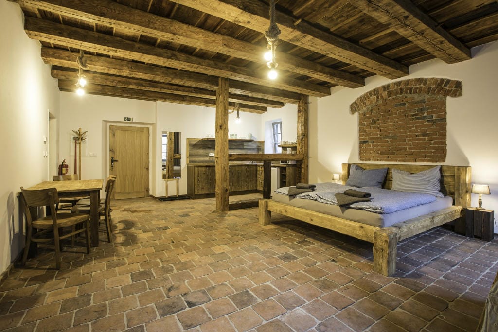 Prostorný apartmán číslo 1 v Klenbách v Třeboni. Na obrázku je vidět stylový interiér s dřevěnými trámi, pohodlnou postelí a přírodním nábytkem, který ladí s historickou atmosférou objektu.