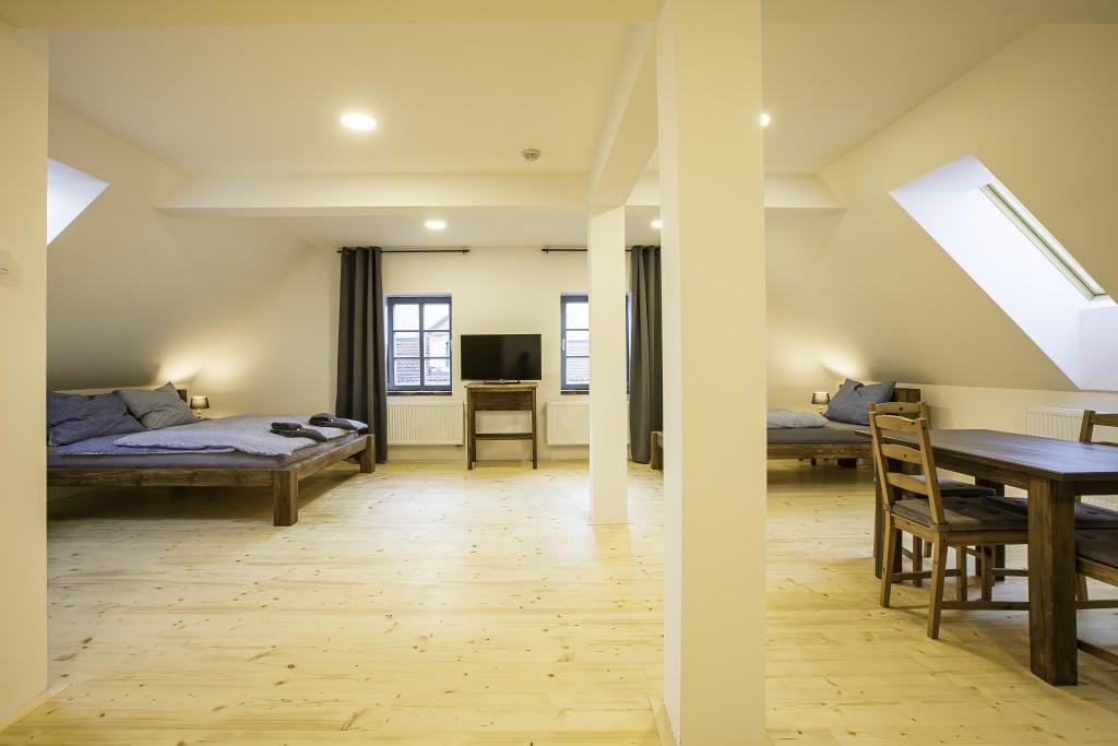 Celkový pohled na uspořádání lůžek a obývací zóny v Apartmánu 3 se světlou podlahou a střešními okny.